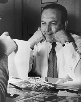 Producers Prints: Film producer Val Lewton smiling as he looks at a photograph