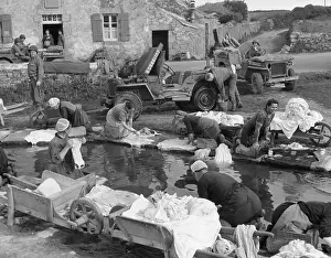 Liberation Prints: French village women doing their share their laundry facility with GI's washing their Jeep