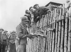 Liberation Prints: GI of the Seventh US Army gives his last cigarettes to liberated Dachau prisoners behind a stockade