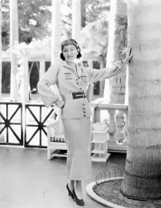 Gloria Prints: Gloria Swanson, modeling a gold wool sports suit with red trim, ca. 1934