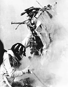 Automobiles Prints: Graham Hill, lifts part of the burning wreckage to clear unconscious Peter Revson