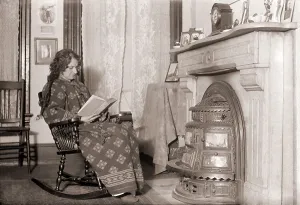Curtains Prints: In a heavy robe, a woman reads in front of a coal stove installed in her fireplace