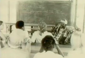 Communes Prints: Henry Mercer teaching school. Written on the blackboard is Black History