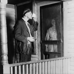 Depression Prints: Homeless man in ragged clothes eating a meal standing as his benefactor keeps her distance behind her front door