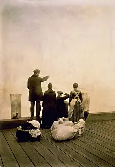 New World Prints: Immigrant family and their belongings on a dock, looking out over the water. Ca. 1912