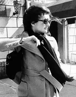 Jacqueline Kennedy Onassis, a recently widowed for a second time, turns her head and raises her arm to avoid a photographer as she leaves her New York apartment building