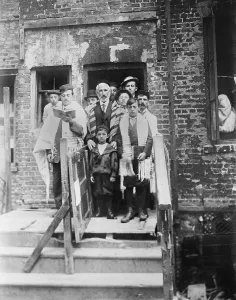 Holidays Prints: Jewish men and boys in prayer shawls standing in front of a dilapidated tenement synagogue on Yom Kippur