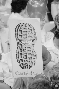 August Prints: Jimmy Carter supporter holding Carter for President sign showing a peanut shell with a toothy grin at the Democratic