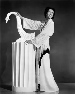 1930s Fashion Prints: Kay Francis modeling white-crepe lounging robe with crimson trim, 1937