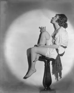 Full length portrait of young woman smoking a cigarette, seated on pedestal, in profile, photograph, 1922