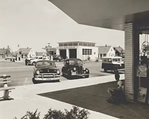 Automobiles Prints: Levittown, N.Y. corner store across the street from a gas station