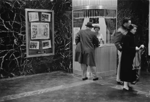 Lobby Prints: Man purchasing a movie ticket from a woman in a ticket booth as a couple stands to the side