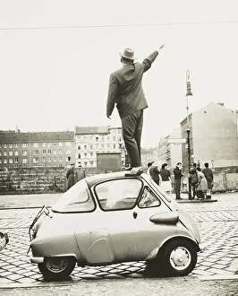 Communism Prints: A man standing on top of a small three-wheeled car waving across the newly constructed Berlin Wall