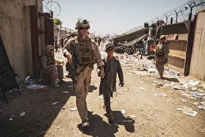 Protection Prints: US Marine escorts an Afghan youth to his family through a fortified enclosure during the evacuation operation at Kabul