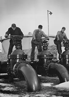 Water Transport Prints: Men turn the wheels of large valves that regulate the flow of oil into oil tankers at a U