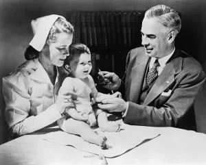 Patients Prints: Nurse holding an infant as a doctor prepares to immunize the child against influenza. 1958