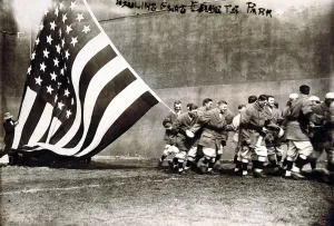 Edwardian Prints: Old Glory. Group of men raising large American flag on opening day of the 1914 baseball season