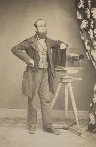 Equipment Prints: Photographers full length portrait standing next to a box camera resting on a tripod in a photo studio