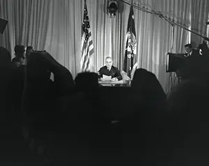 Reporters Prints: President Harry Truman seated at his desk with lights on and cameras rolling