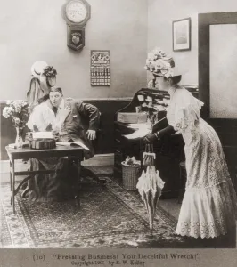 Secretaries Prints: PRESSING BUSINESS YOU DECIETFUL WRETCH Is the caption to a photo of a woman surprising husband who is embracing
