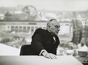 Moses Prints: Robert Moses in 1964, seated at a table with a view of the New York Worlds Fair in the distance