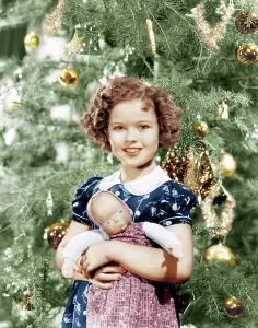 Temple Prints: Shirley Temple holding doll by Christmas tree, ca. late 1930s