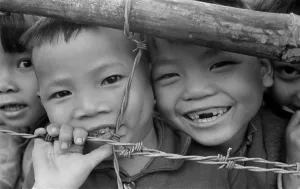 War Victims Prints: Smiling youngsters press against a barbed wire fence