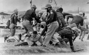 April Prints: SNCC leader John Lewis (light coat in center) cringes as an Alabama State Trooper swings his club at Lewis head