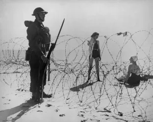 Bathing Suits Prints: Soldier standing guard next to barbed wire barricade on an English beach during World War 2