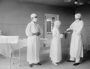 Doctors Prints: Surgical nurse assists surgeons into rubber gloves before an operation