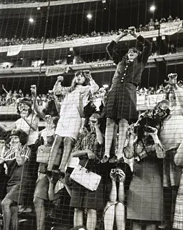 Excitement Prints: Teenage girls climb a wire fence to get a better view of the British singing group