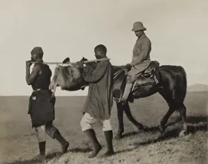 Shot Prints: Theodore Roosevelt rides beside African porters carrying an lion skin back to camp
