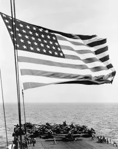 Aircraft Carriers Prints: U.S. flag waving in foreground over flight deck of an escort carrier on July 16, 1943