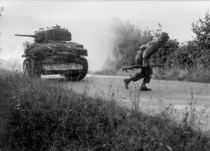 Hedgerows Prints: U.S. soldier crosses a road cautiously under the cover of a light tank in the Hedgerows of Normandy