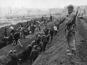 Guard Prints: U.S. Soldier guards the reburial of concentration camp victims by German civilians