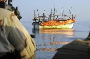 Candid Occupational Portraits Prints: Back view of U.S. sailors with weapons ready as they approach a ramshackle dhow in the Gulf of Aden