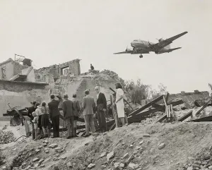 West Berliners gathered near war ruins in Berlin watch a U.S. Air Force transport plane