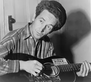 Woody Guthrie (1912-1967), folk singer playing a guitar that has a sticker attached reading: This Machine Kills Fascists