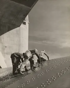 Three workers painting on a slanted wall of riveted-steel plates on the Hoover Dam spillway. Ca. 1940