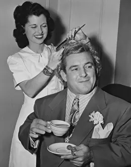 World Champions Prints: Wrestler Gorgeous George holding a tea cup as his hair is styled by Miss Bettie of Hollywood