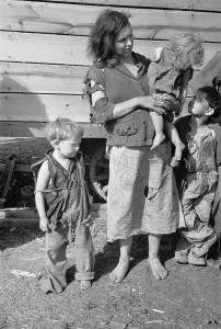 Shack Prints: Young mother dressed in a ragged sweater and a skirt made of a flour sack with three children also dressed in rags